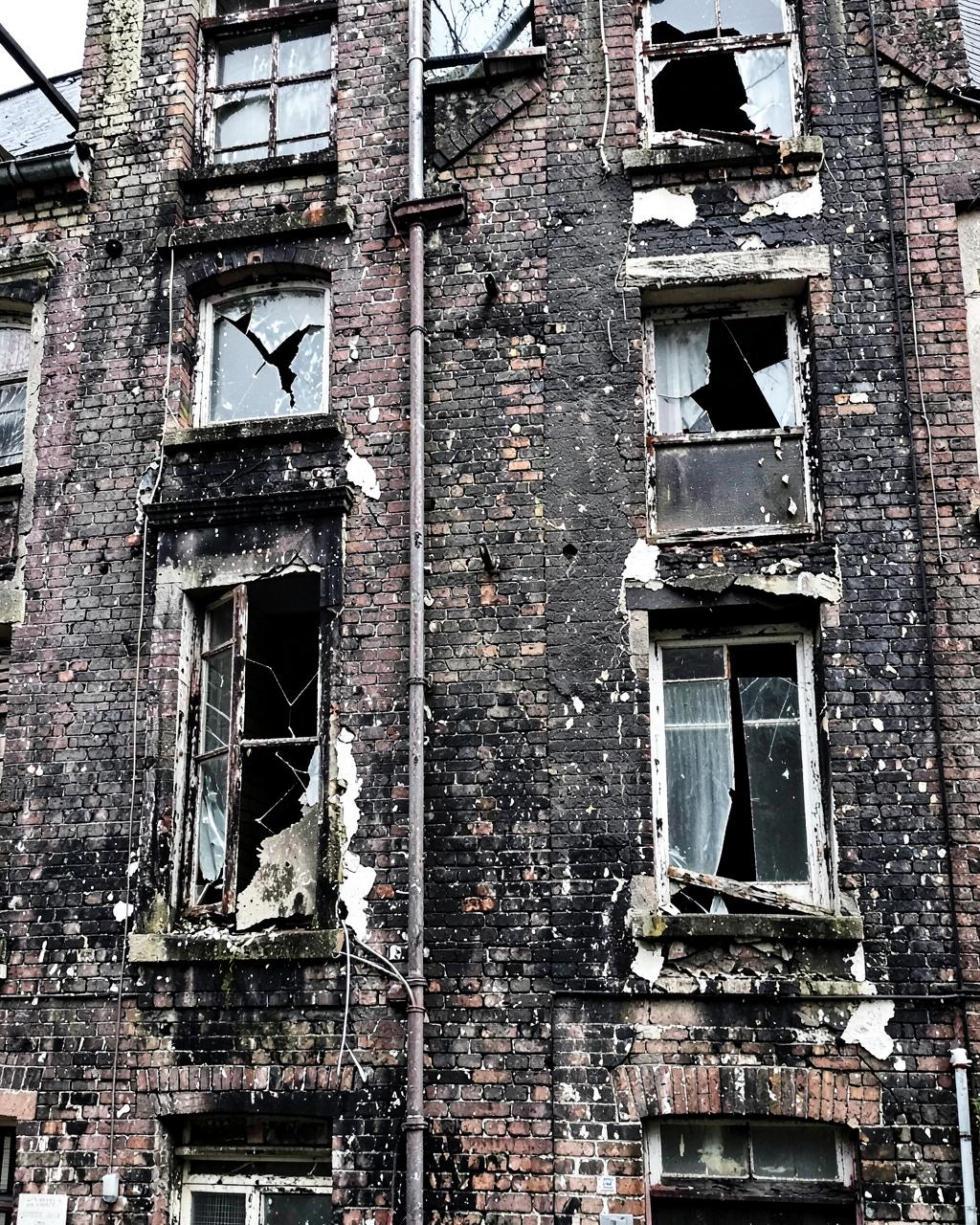 Façade en briques noircies, châssis pourris et vitres cassées